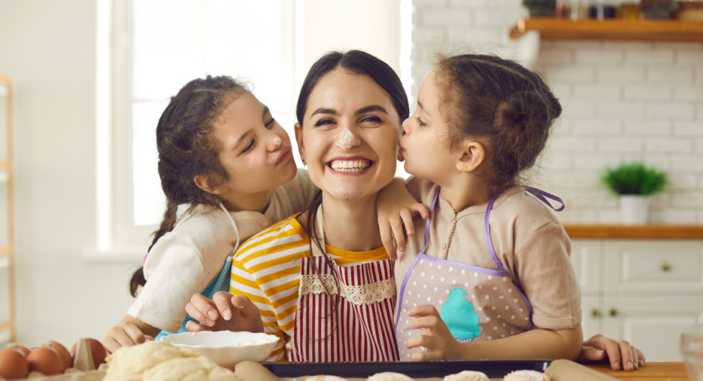 zwei kleine Kinder in der Küche die Ihre Mutter auf die Wangen küssen