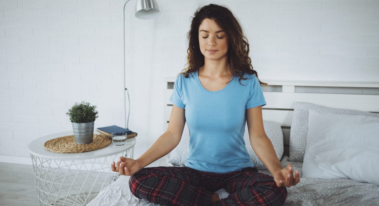 Beautiful woman sitting on her bed and meditating alone during the morning at home